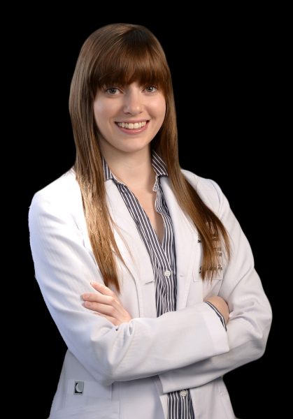 Portrait professionnel d’une dentiste en sarrau blanc, souriante, sur fond noir.